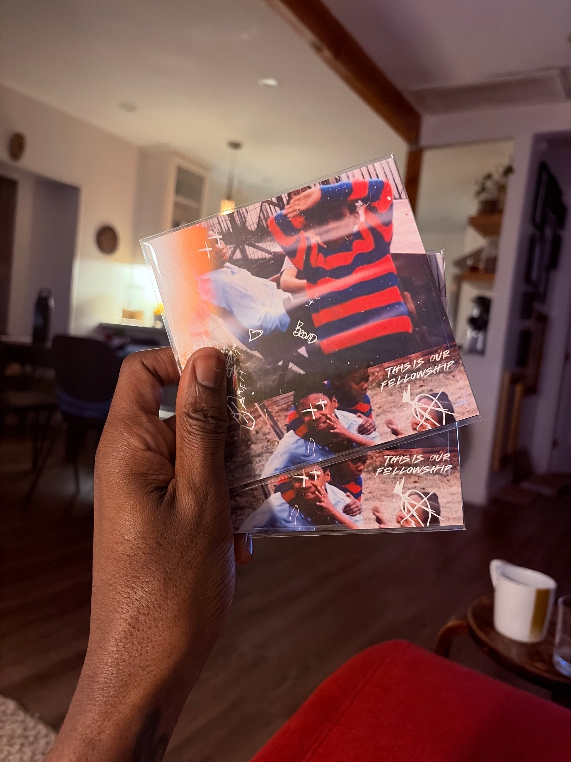 Hand holding a photo album with images of a person in a striped shirt in a living room setting.